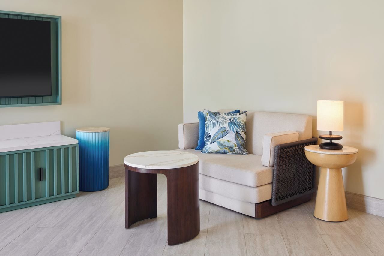 A modern living room with a sofa, two side tables, a blue trash bin, and a wall-mounted TV.