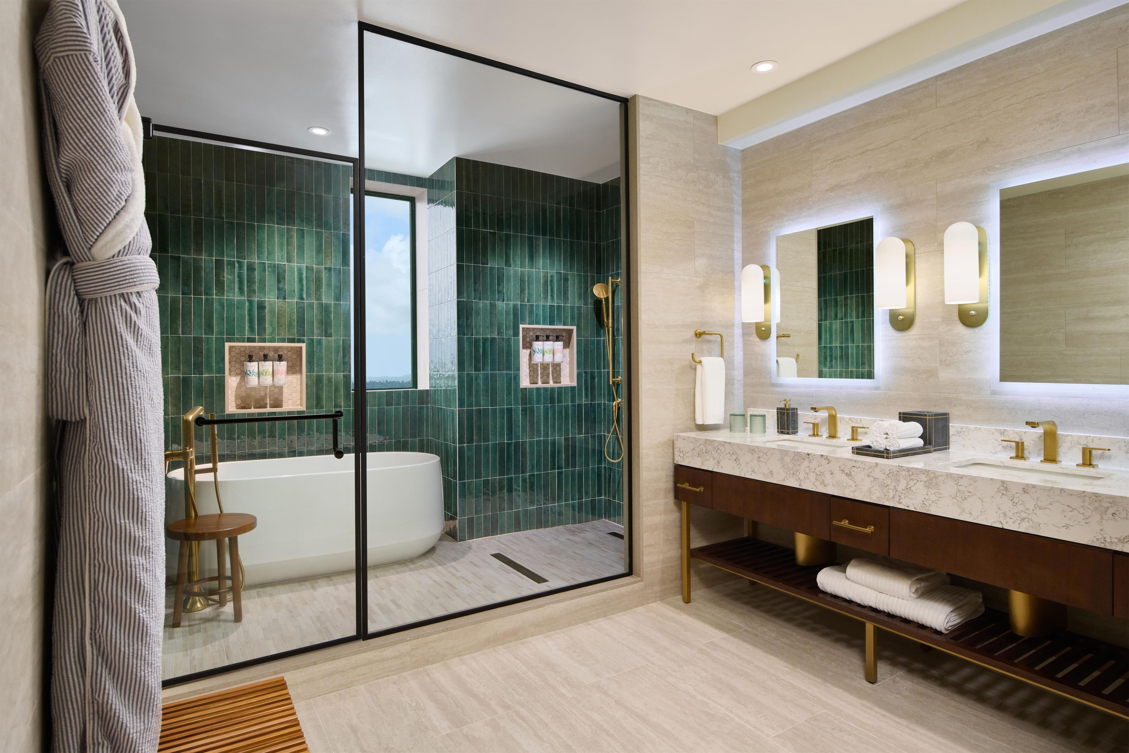 A modern bathroom with a glass shower enclosure, a bathtub, a vanity with a marble countertop, and a large mirror with wall sconces.