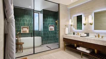 A modern bathroom with a glass shower enclosure, a bathtub, a vanity with a marble countertop, and a large mirror with wall sconces.