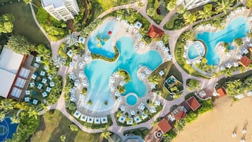 Vue aérienne d’un complexe hôtelier doté de plusieurs piscines, d’espaces de détente et d’une plage.