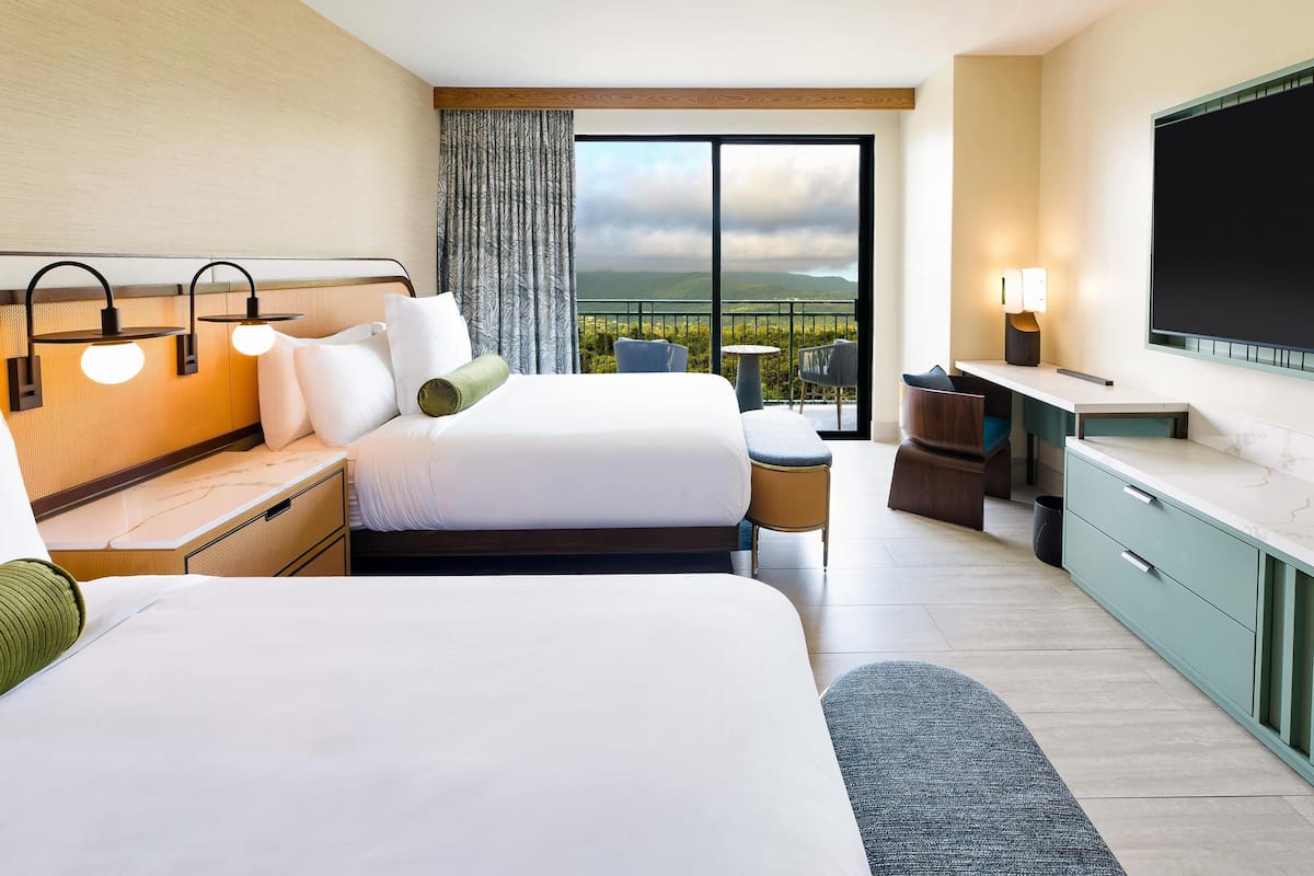 A hotel room with two beds, a desk, a chair, a TV, and a balcony with a view.