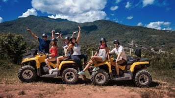 Un grupo de personas manejando vehículos todo terreno en un entorno natural, con montañas al fondo.