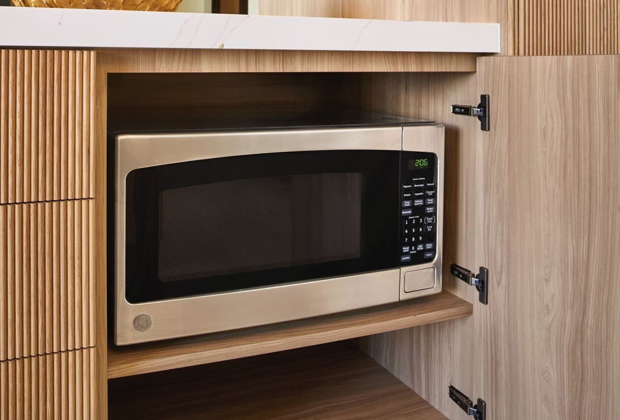 A microwave oven built into a wooden cabinet with a digital display.