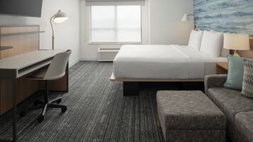 A hotel room with a bed, a desk with a chair, a television, a window with a view, and a wall with a blue pattern.