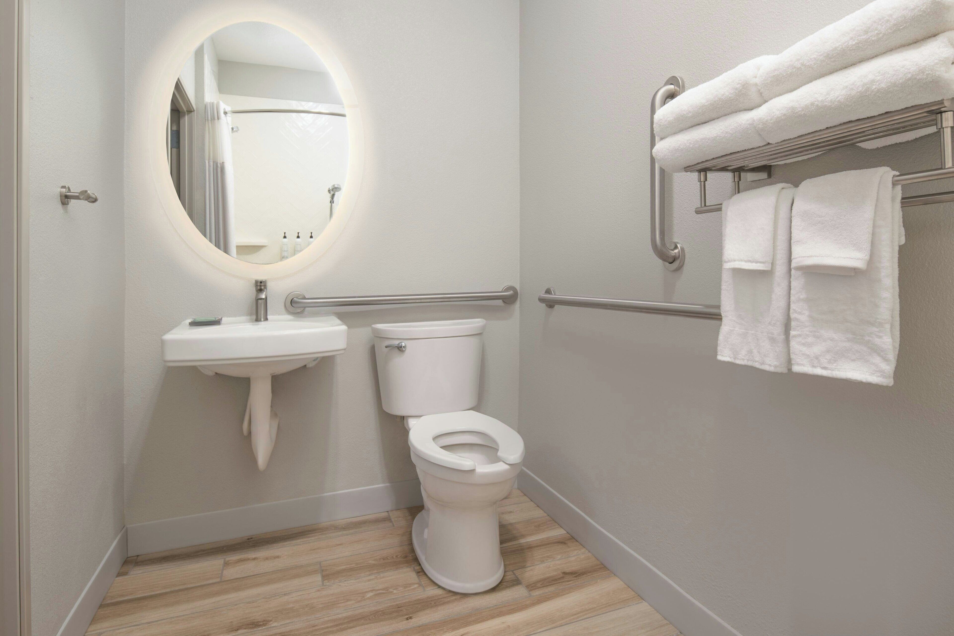 A bathroom with a toilet, sink, and handrails.