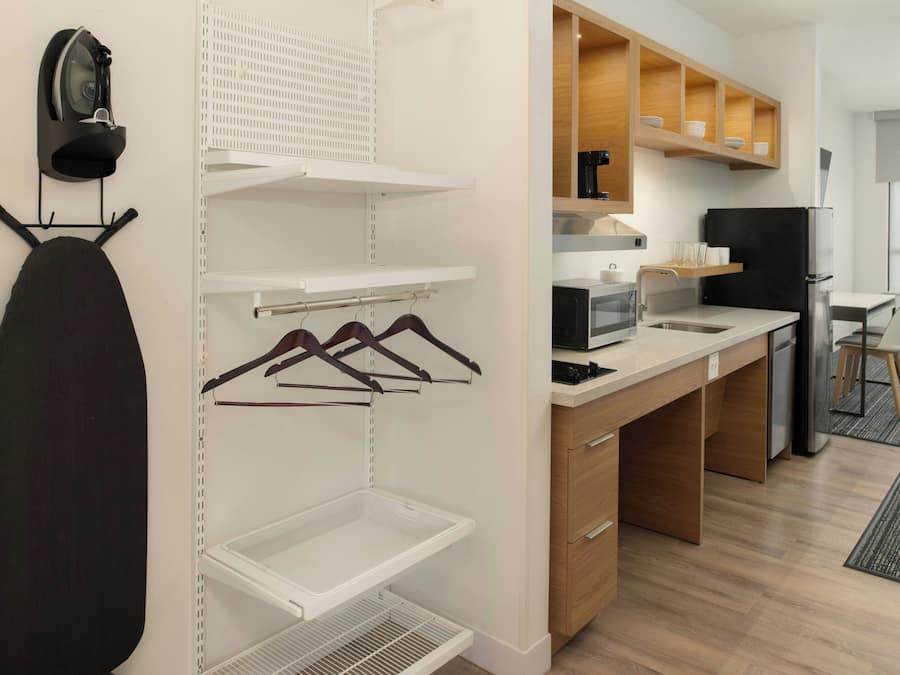 A modern kitchen with wooden cabinets, a black refrigerator, and a microwave. There is a hanging iron and a drying rack on the wall.