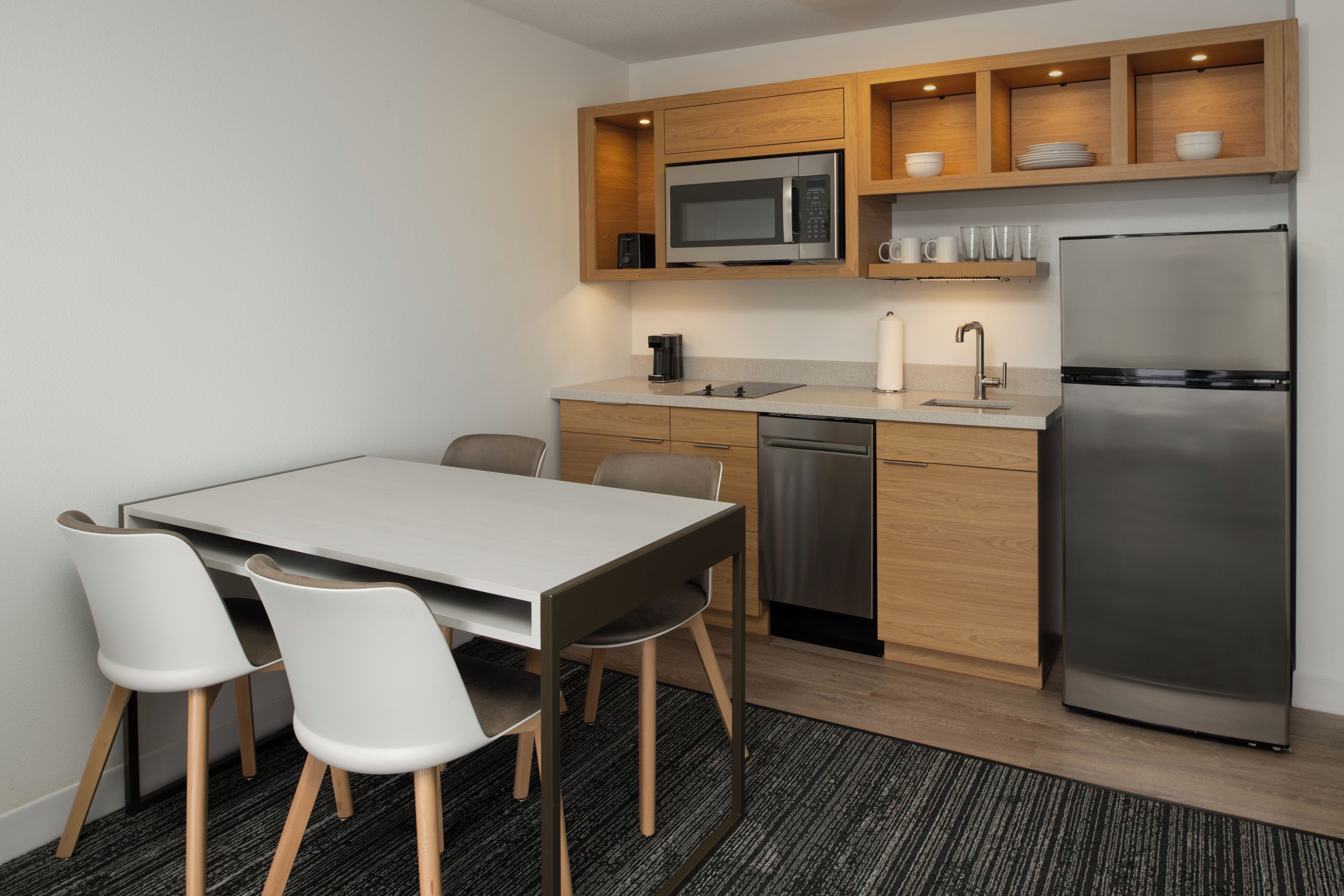A modern kitchen with a stainless steel refrigerator, a microwave, and a dishwasher. There is a dining table with four chairs.