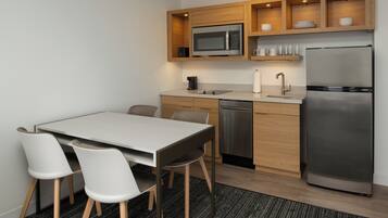 A modern kitchen with a stainless steel refrigerator, a microwave, and a dishwasher. There is a dining table with four chairs.