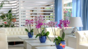 A modern living room with a white sofa, two blue coffee tables, and potted plants. - Hotel Caravel (Sant'Agnello)
