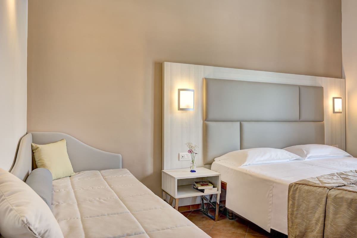 A hotel room with a bed, a bedside table with a lamp, and a nightstand with a book.