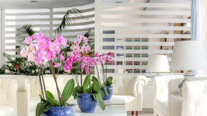 A modern interior with white leather sofas, blue planters with pink orchids, and a white lamp. - Hotel Caravel (Sant'Agnello)
