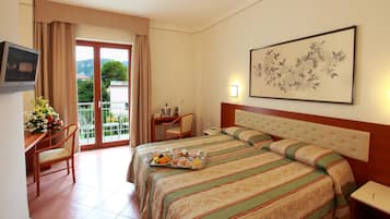 A hotel room with a bed, a desk with a chair, a small table with a lamp, and a balcony with curtains.