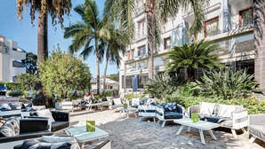 An outdoor seating area with sofas and tables, surrounded by palm trees and plants. - Hotel Caravel (Sant'Agnello)
