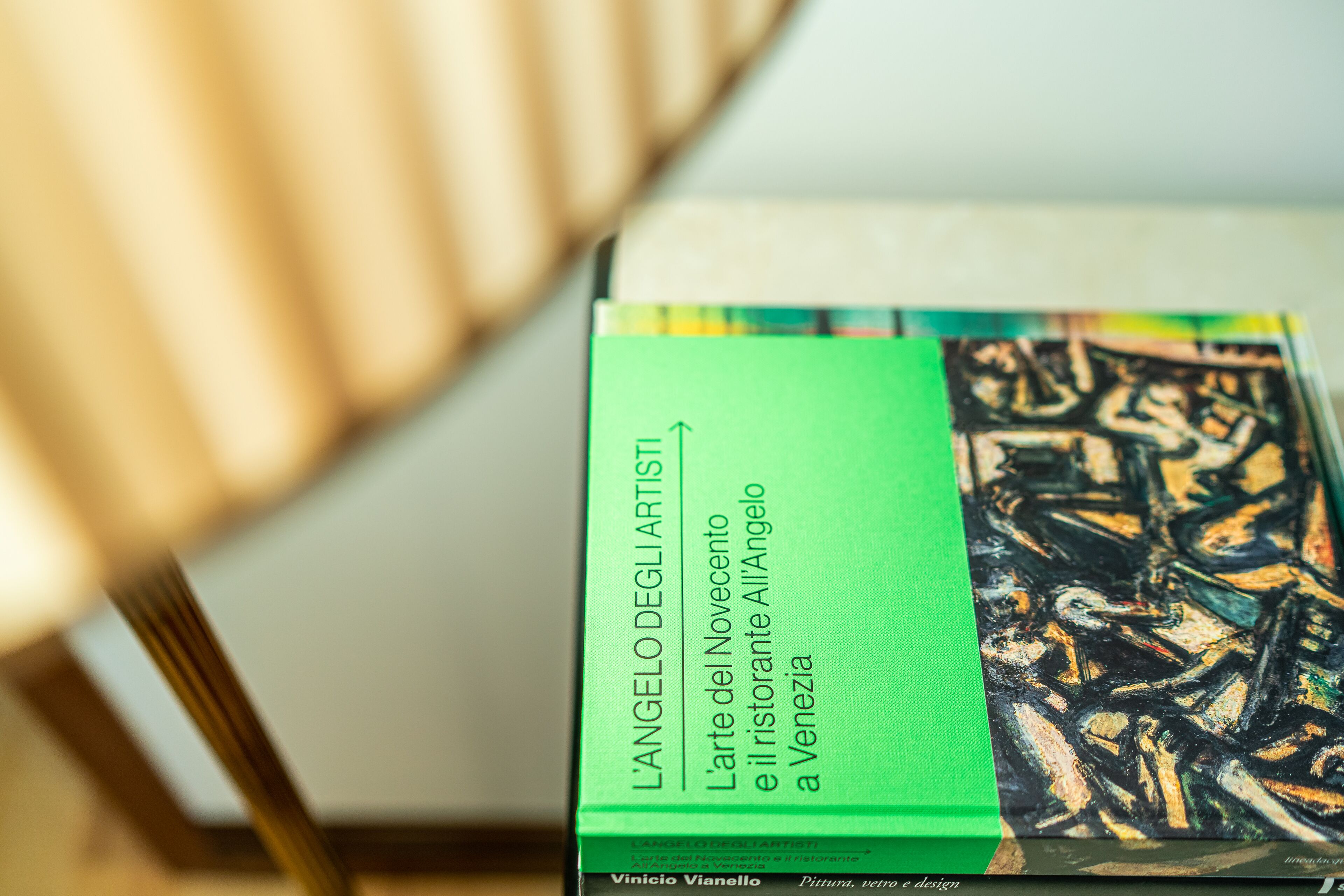 A book titled 'L'ANGELO DEGLI ARTISTI' by Vinicio Vianello, with a green cover and an abstract painting on the back.