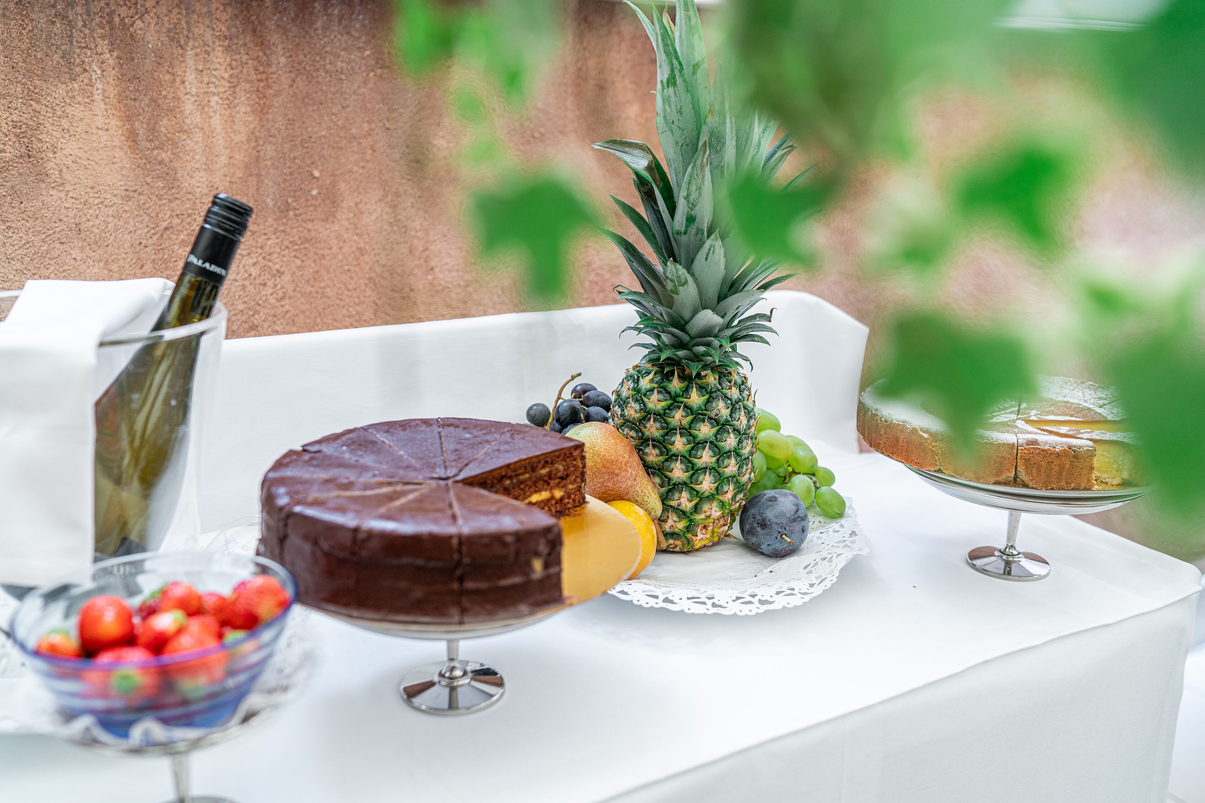 A table with a chocolate cake, a pineapple, grapes, a loaf of bread, and a bowl of strawberries.