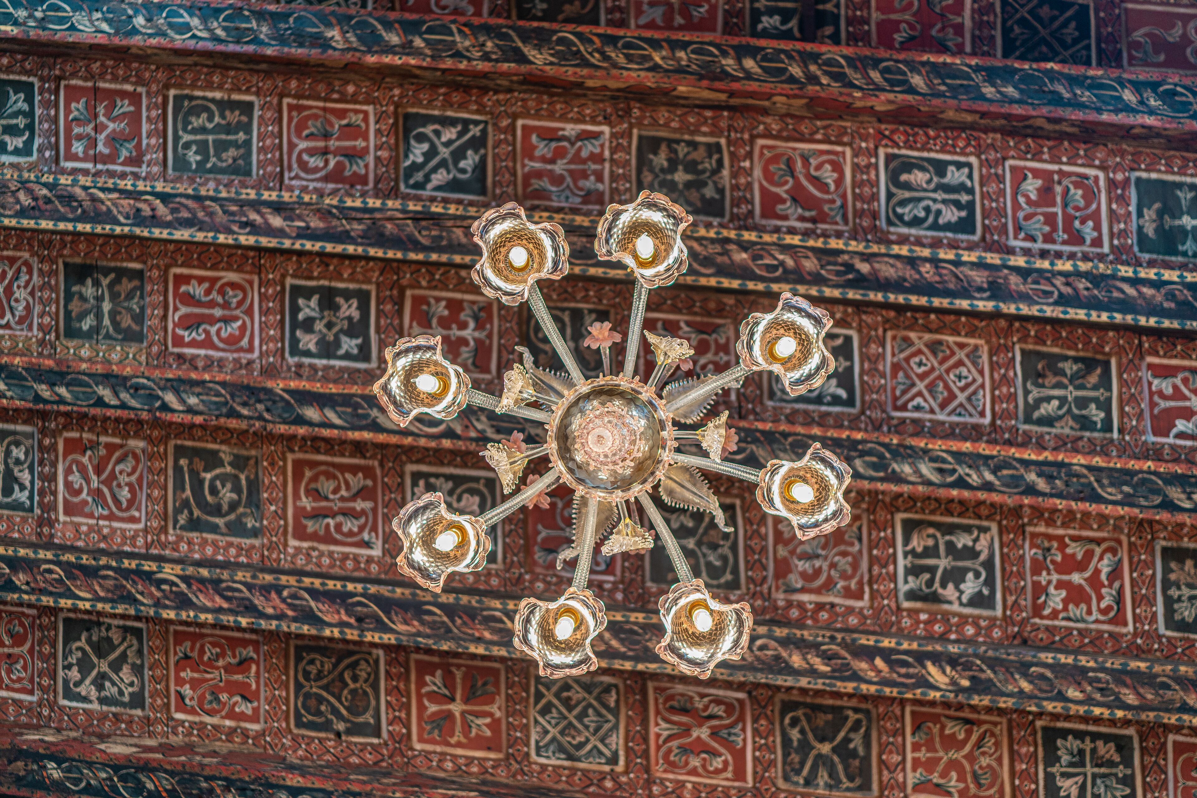 A chandelier with multiple arms and lights, set against a wall with intricate tile patterns.