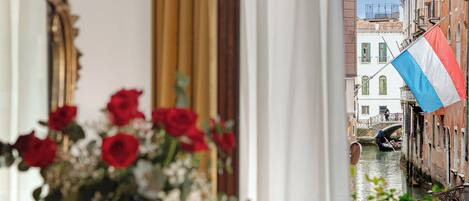 A room with a view of a canal, a table with a vase of red roses, and a mirror.