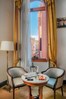 A room with two upholstered chairs, a table with a fruit platter, a lamp, and a window with curtains.