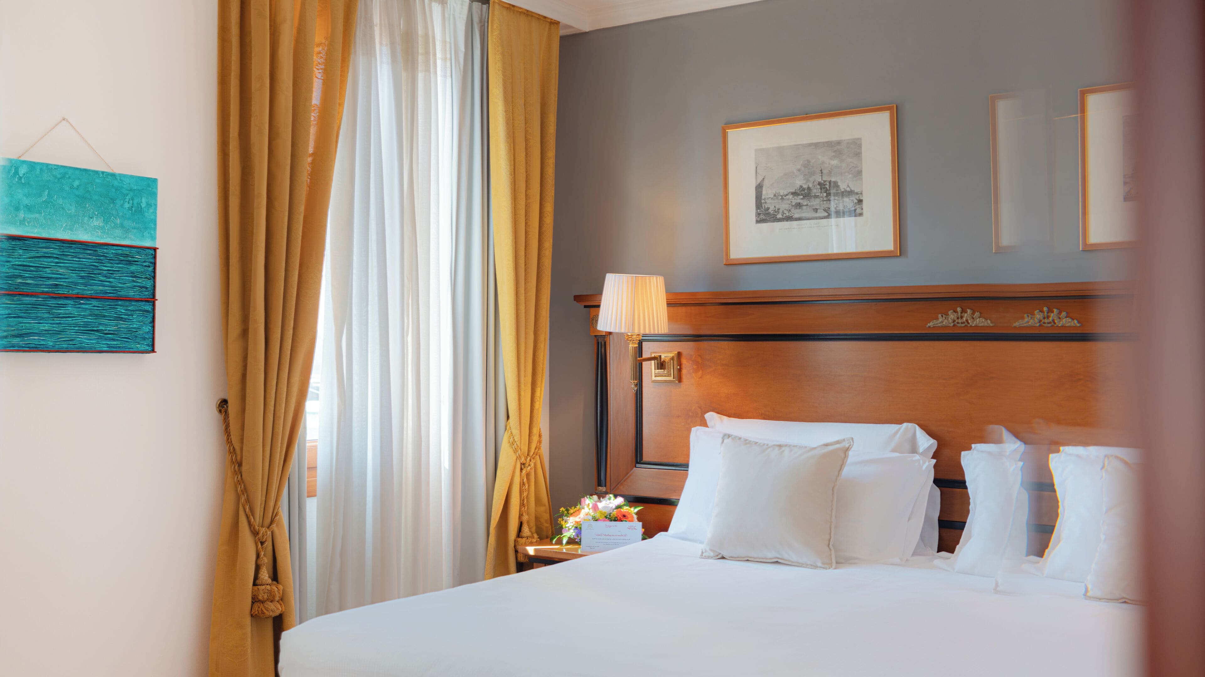 A hotel room with a large bed, a wooden headboard, a nightstand with a lamp, and a framed picture on the wall.