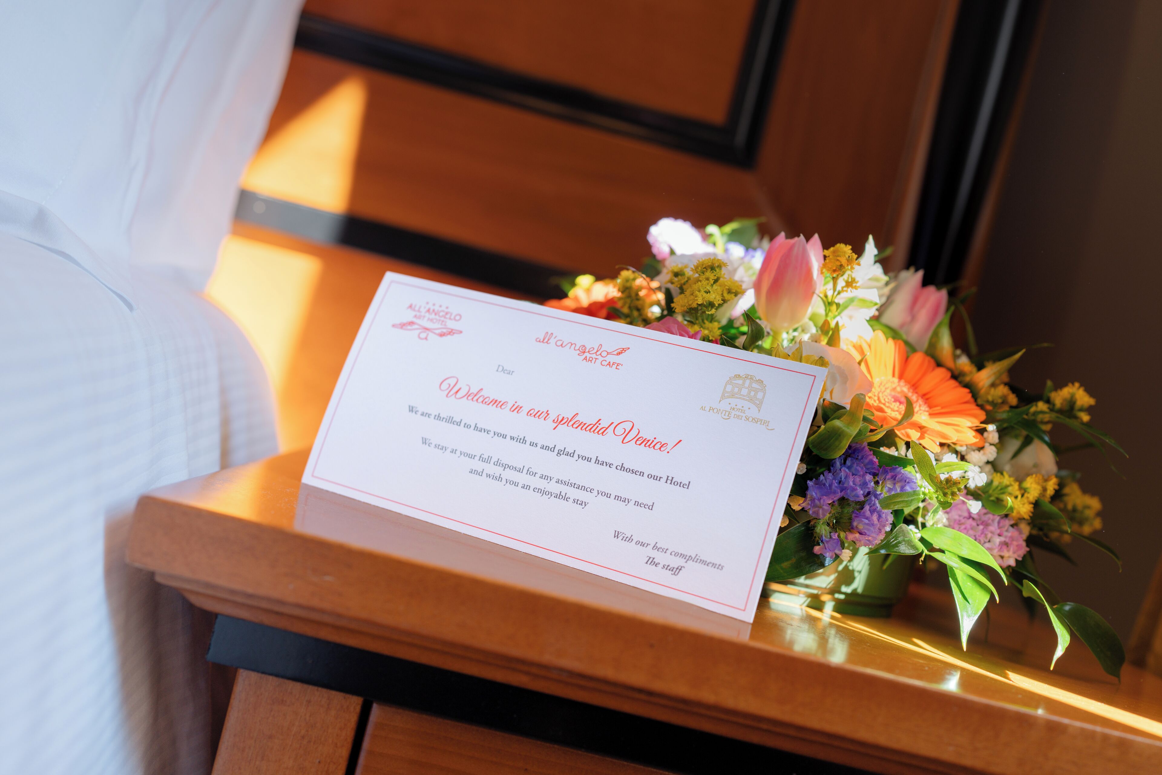 A welcome card and a floral arrangement on a wooden table.