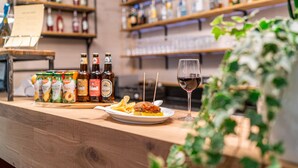 Un comptoir de bar avec une variété de bouteilles, une assiette de nourriture et un verre de vin rouge.