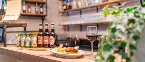 Um balcão de bar com diversos frascos, um prato com comida e um copo de vinho tinto.