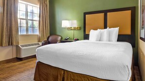 Habitación de hotel con una cama grande, un escritorio con lámpara, una silla y una ventana con cortinas.