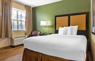 A hotel room with a large bed, a desk with a lamp, a chair, and a window with curtains.