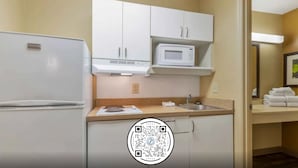 Una cocina compacta con armarios blancos, un microondas y un refrigerador.