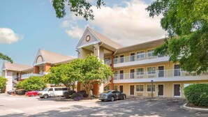 Un hotel de varios pisos con un atrio central, balcones en los pisos superiores y un estacionamiento con varios autos.