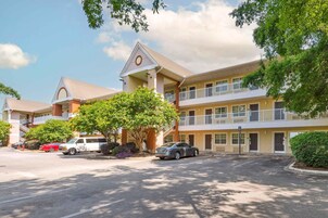 A multi-story hotel with a central atrium, balconies on the upper floors, and a parking lot with several cars.