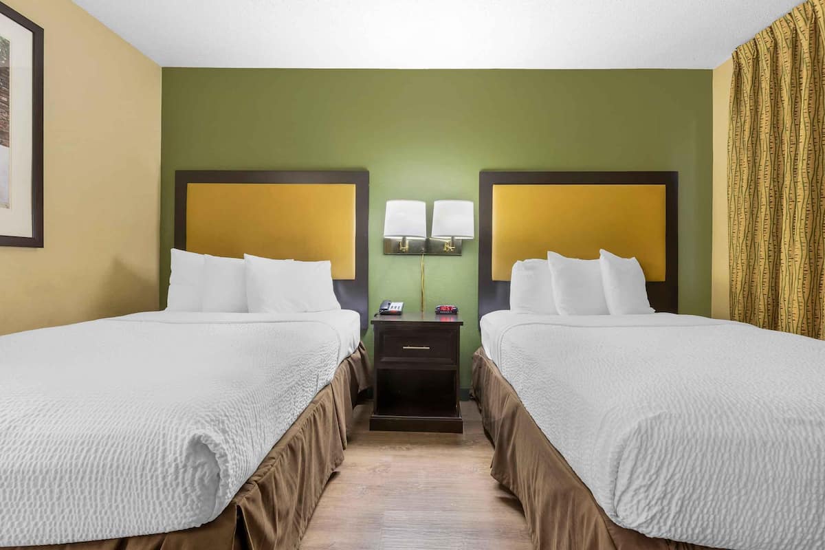 Ein Hotelzimmer mit zwei Betten, einem Nachttisch mit Lampe und einem gerahmten Bild an der Wand.