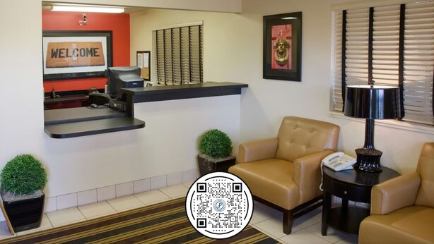 Un área de recepción con un cartel que dice 'WELCOME', un mostrador, dos sillas, una lámpara y un código QR en el suelo.