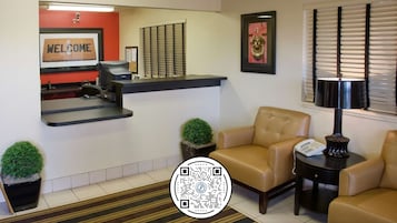 A reception area with a 'WELCOME' sign, a desk, two chairs, a lamp, and a QR code on the floor.