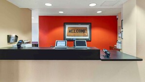 Un mostrador de recepción con una pared roja, un cartel de bienvenida y dos computadoras portátiles.