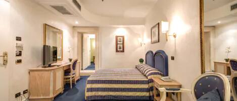 Una habitación de hotel con cama, escritorio, silla, espejo y televisión.