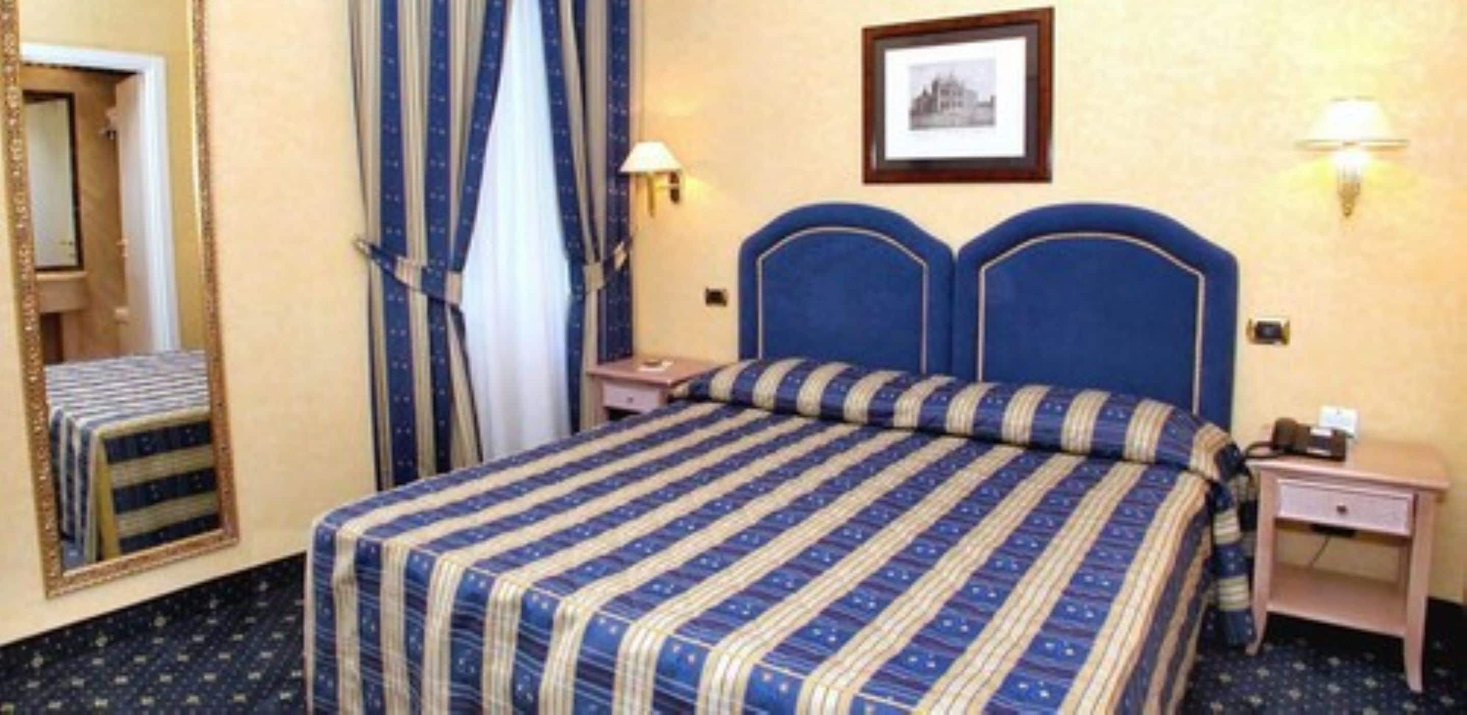 Een hotelkamer met een groot bed, twee nachtkastjes, een spiegel en een ingelijste foto aan de muur.
