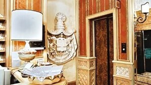 A room with a wooden vanity, a mirror, a decorative wall panel, and a door with a handle. - Hotel Valle (Rome)