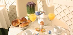 A breakfast table with croissants, orange juice, a teapot, and a vase of flowers. - Hotel Valle (Rome)