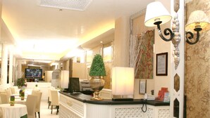 A hotel lobby with a reception desk, a television, a decorative plant, and a patterned wall. - Hotel Valle (Rome)