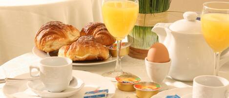 A breakfast setting with croissants, orange juice, a teapot, and a cup of coffee on a table.