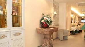 A hotel corridor with a decorative fountain, a glass display cabinet, and a seating area with tables and chairs. - Hotel Valle (Rome)