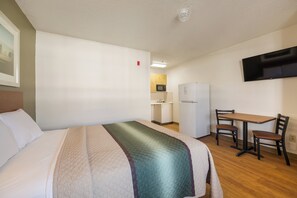 A hotel room with a bed, a desk, a chair, a television, and a kitchenette. - HomeTowne Studios by Red Roof Spartanburg - Asheville Highway (Spartanburg)