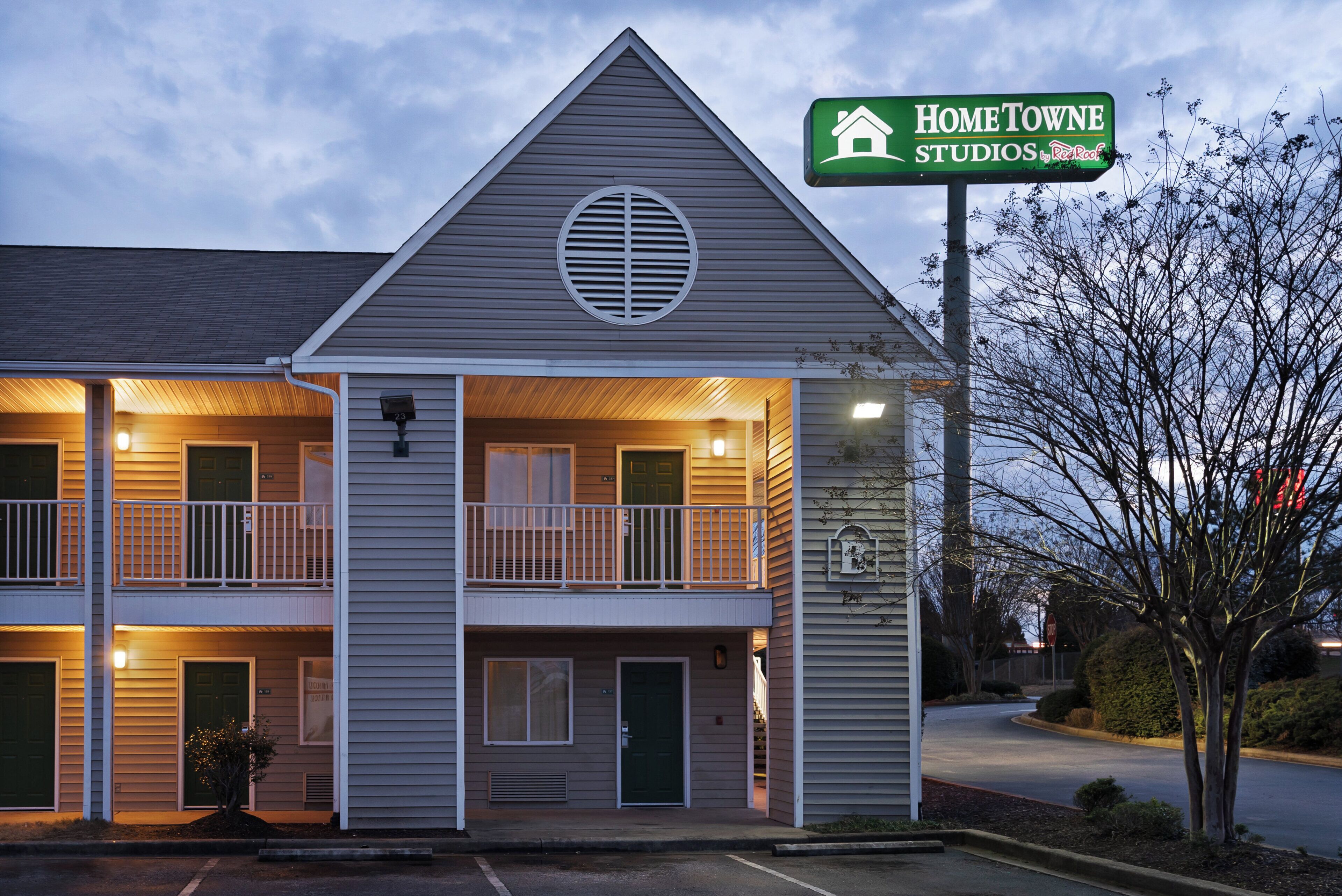 Een motel met twee verdiepingen, met een groen bord waarop 'HOMETOWNE STUDIOS by Red Roof' staat.