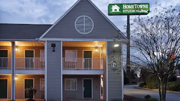 Een motel met twee verdiepingen, met een groen bord waarop 'HOMETOWNE STUDIOS by Red Roof' staat.