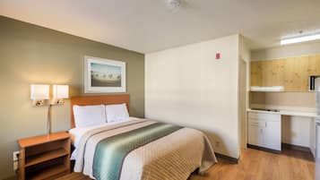 A hotel room with a bed, bedside lamps, a painting, a small desk, and a kitchenette.