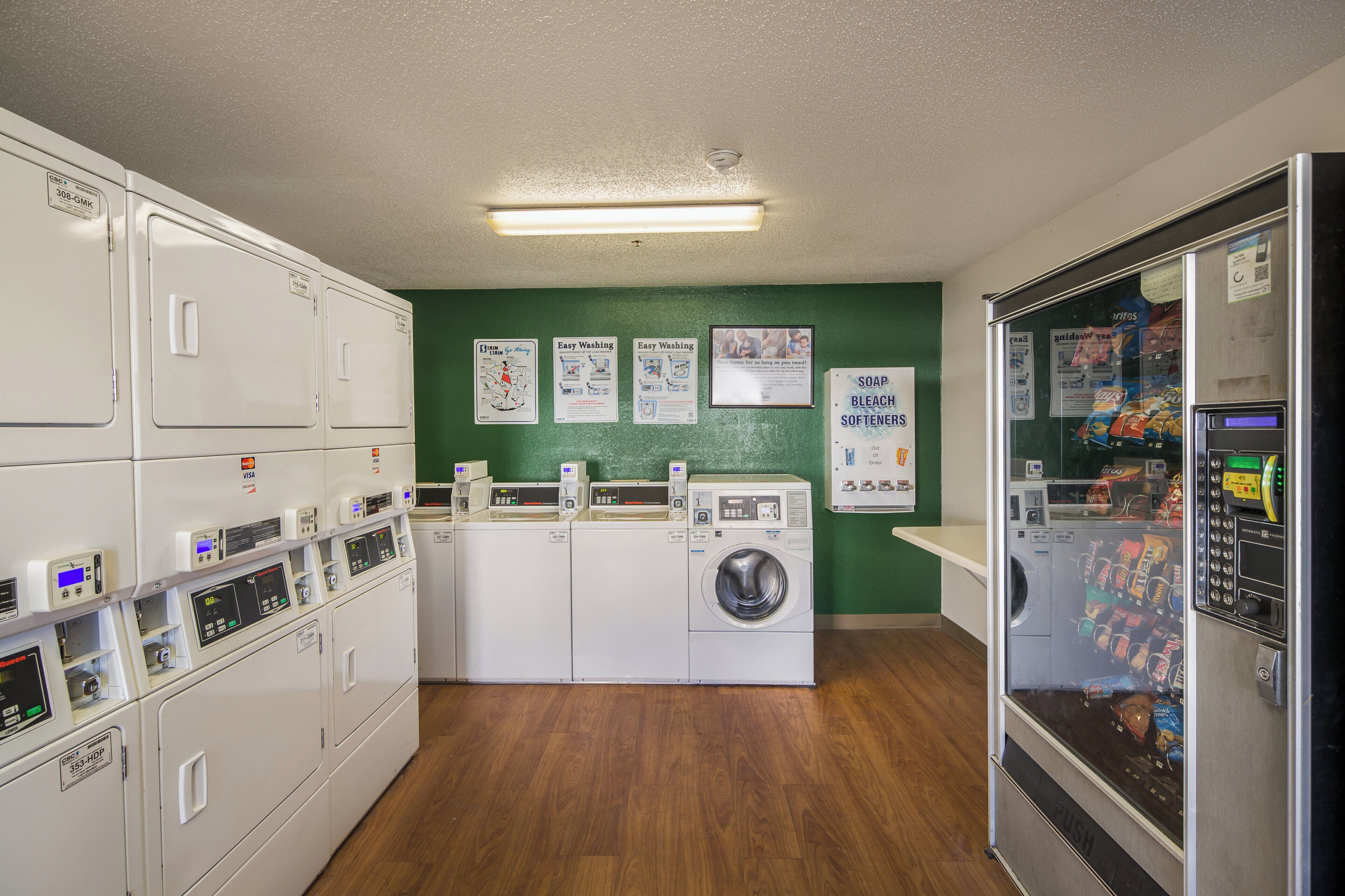 A laundry facility with multiple washing machines, dryers, and a self-service vending machine.