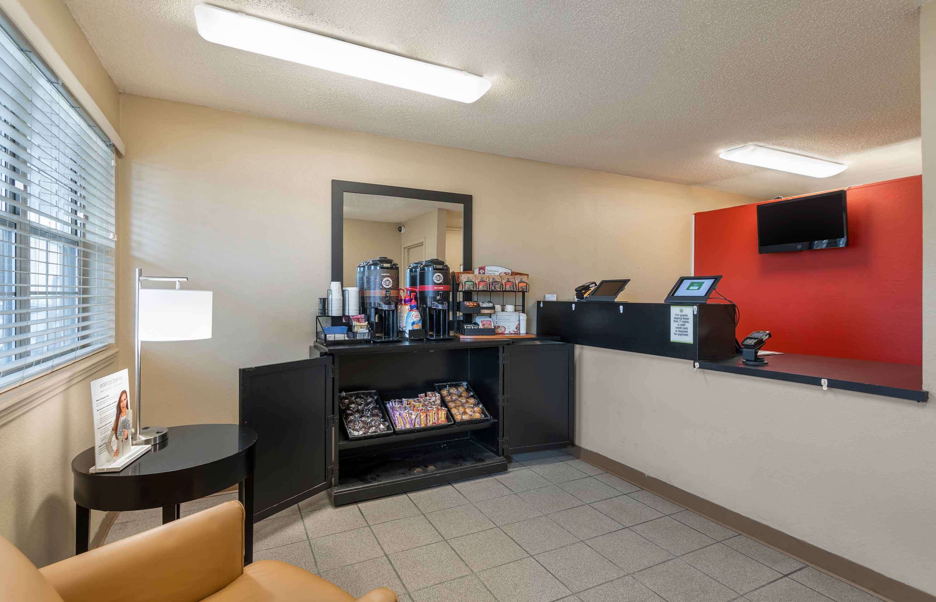 Eine Hotelhalle mit Empfangsschalter, Kaffeeautomaten, einem Fernseher und einer Sitzecke.
