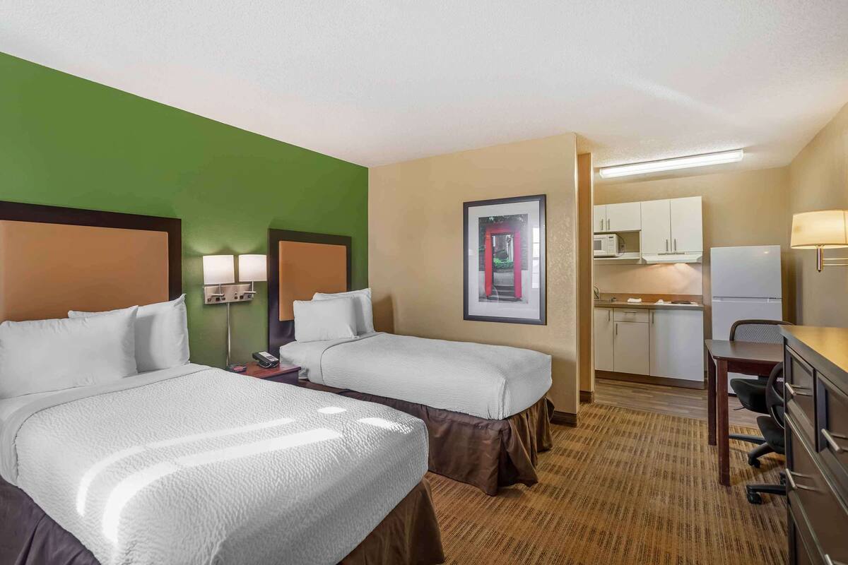 Ein Hotelzimmer mit zwei Betten, einer Küchenzeile und einem Schreibtisch mit Stuhl.