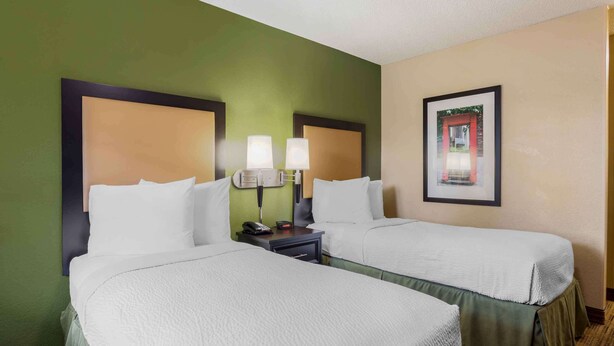 A hotel room with two beds, green walls, a framed picture, and a nightstand with a lamp. - Extended Stay America Select Suites - Chattanooga - Airport (Chattanooga)